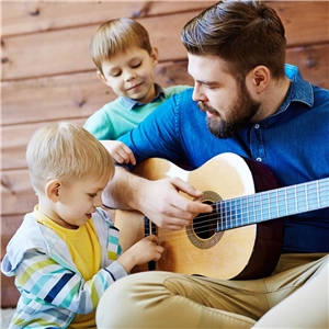 Erzieher spielt Gitarre und zwei kleine Jungs hören zu