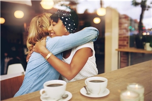 zwei Frauen umarmen sich, vor ihnen stehen zwei Tassen Kaffee