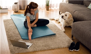 Frau auf Yogamatte vor Laptop