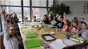 Die Kinder des Kinderbeirates sitzen an einem Tisch voller Unterlagen und strecken die Hände zum Abstimmen in die Höhe.