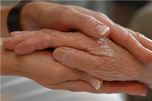 Die Hände einer Jungen Frau umschließen die Hand einer alten Person