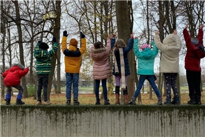 Acht Kinder stehen auf einer Mauer.