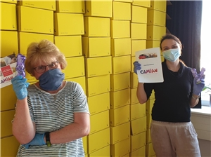 Zwei Frauen mit Atemschutzmasken stehen vor Paketwand