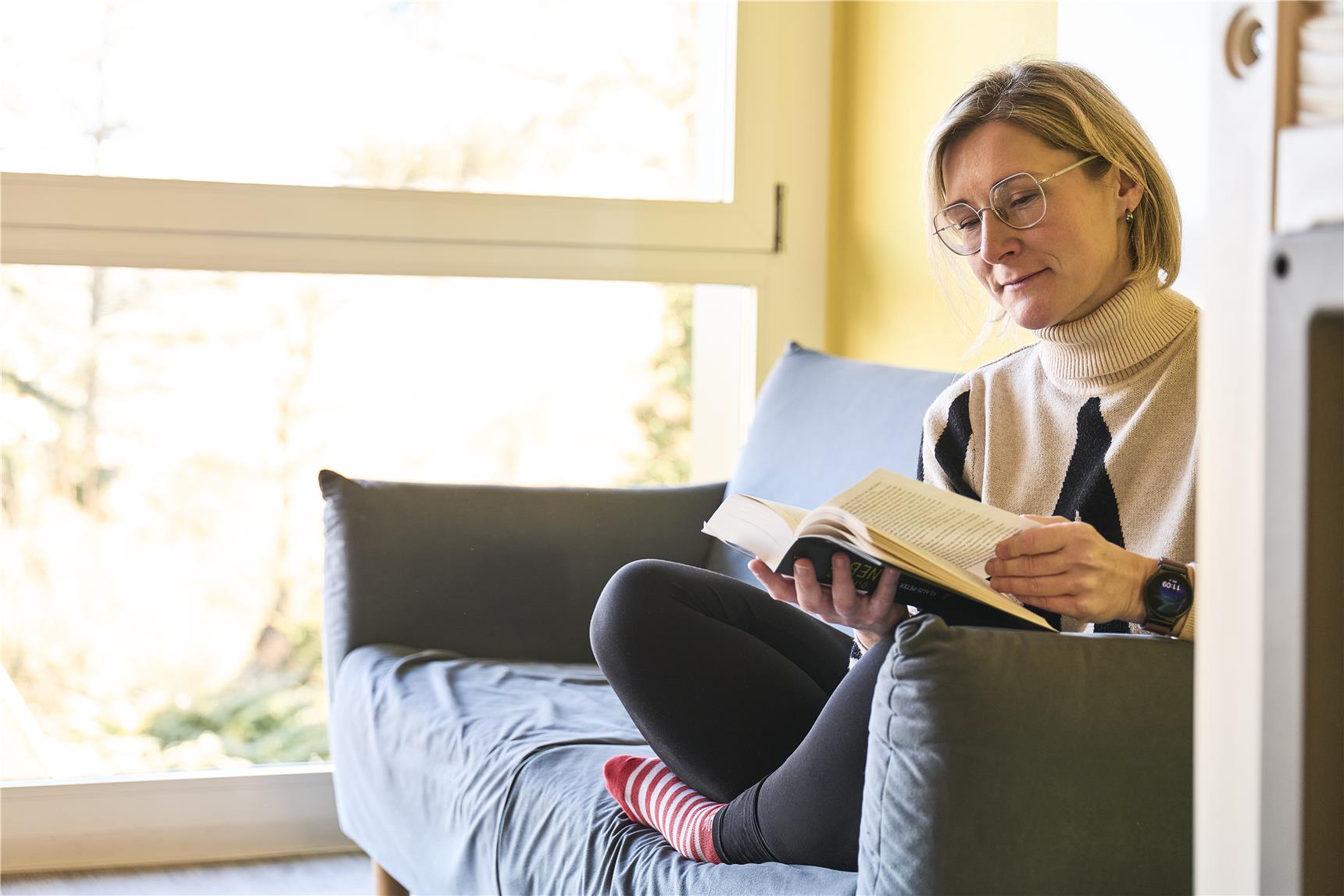 Frau liest auf einem Sofa ein Buch