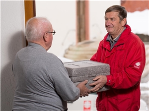Caritasmitarbeiter bringt älterem Mann Essensbox