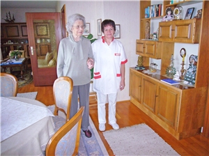 Pflegerin führt ältere Frau an der Hand durch Wohnzimmer