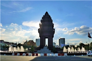 Kambodscha, Phnom Penh Das Denkmal der Unabhängigkeit in Phnom Penh steht auf einem Platz mit Springbrunnen. Das Monument verdeckt die Sonne, am Himmel sind kaum Wolken zu sehen.