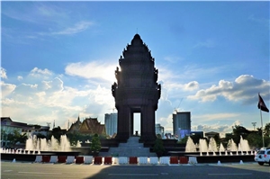 Das Denkmal der Unabhängigkeit  in Phnom Penh steht auf einem Platz mit Springbrunnen. Das Monument verdeckt die Sonne, am Himmel sind kaum Wolken zu sehen.