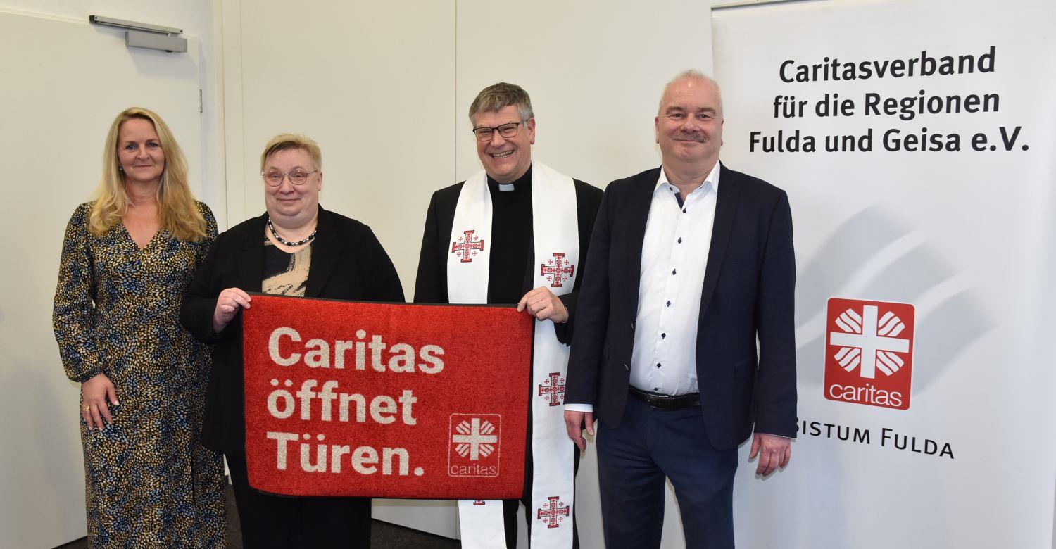 Gruppe steht beisammen mit Fussmatte in der Mitte mit Jahresmotto "Caritas öffnet Türen"