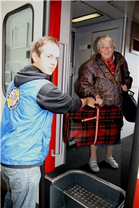 Mitarbeiter hilft älterer Dame mit Koffer
