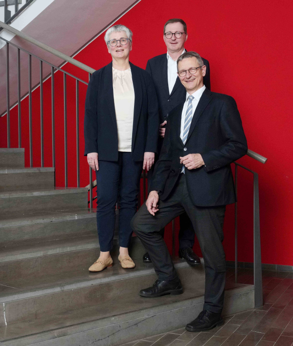 Auf dem Foto siehst Du drei Personen.  In der Mitte steht Dr. Matthias Berger.  Links von ihm steht Yvonne Fritz.  Rechts von ihm steht Dr. Frank Johannes Hensel.