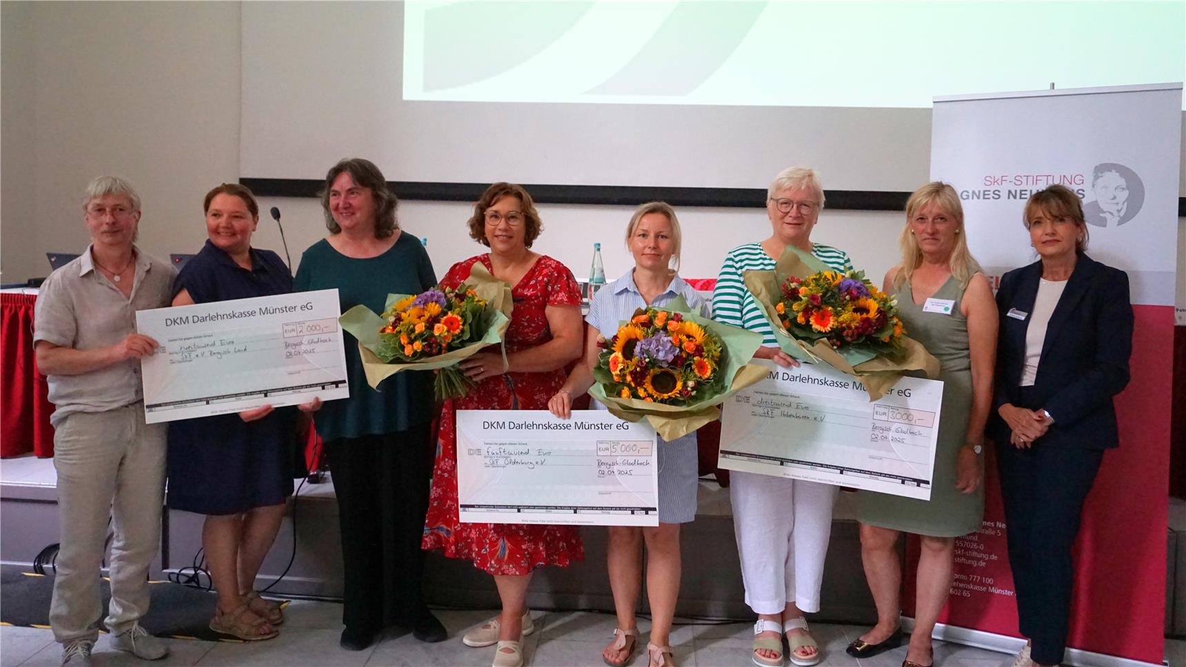 Mehrere Menschen mit Blumen und Gewinnschecks.