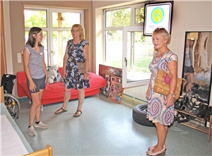 Zwei Besucherinnen und eine Mitarbeiterin bei einer Führung durch Räume der Wohngruppe. Besucherin Elisabeth Durak (rechts) steht in einem Zimmer in der Wohngruppe und schaut sich um. Mit ihr sind noch eine weitere Besucherin und eine Mitarbeiterin im Raum.