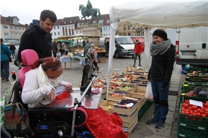 Eine Frau im Rollstuhl ist mit einem Begleiter auf dem Wochenmarkt unterwegs und kann mit Hilfe der Unterstützten Kommunikation ihre Wünsche äußern. Eine Frau im Rollstuhl ist mit einem Begleiter auf dem Wochenmarkt unterwegs und kann mit Hilfe der Unterstützten Kommunikation ihre Wünsche äußern.