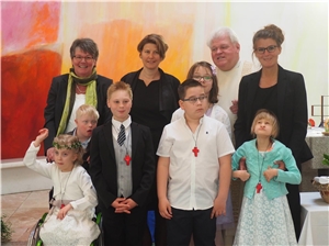 Die sechs Schüler stehen für ein Foto gemeinsam mit der Schulgemeinschaft und dem Schulpfarrer zusammen und freuen sich über ihre Kommunion.
