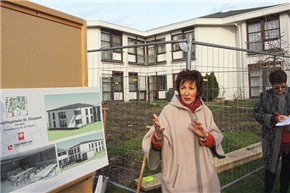 Rednerin vor Bauzaun, daneben Schaubilder der neuen Gebäude