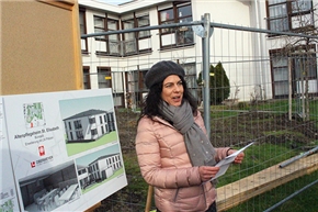 Rednerin vor Bauzaun, daneben Schaubilder mit Grafiken der neuen Gebäude