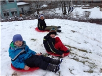 Drei Schüler fahren mit einem Plastik-Bob einen Schneehang herunter