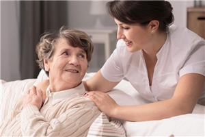 Eine Pflegerin beugt sich beim Schieben des Rollstuhles liebevoll zu einer Seniorin.