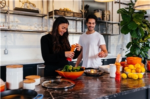 Auf dem Bild sind zwei Menschen zu sehen die in der Küche stehen und ihr Essen würzen.