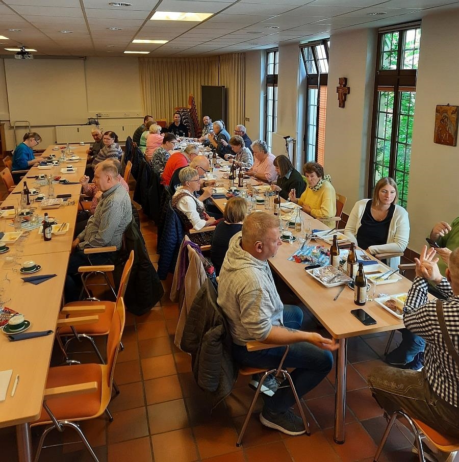 wir blicken in einen großen Raum in dem viele Menschen an 2 Tischreihen platz genommen haben. (Caritas Fulda)