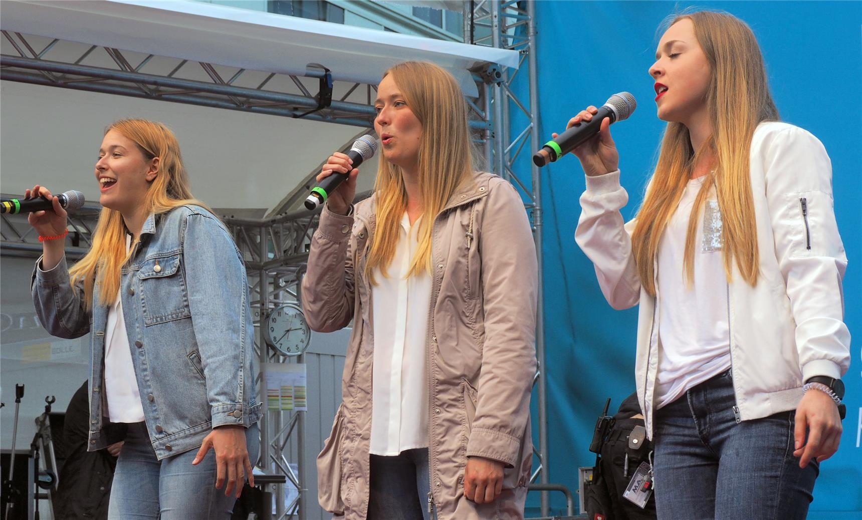 Drei Frauen halten ein Mikrofon und singen. 