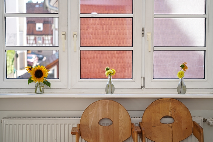 Fenster mit Blick auf Fachwerkhäuser, davor drei Blumenvasen und darunter die Lehnen zweier Kinderstühle (Caritasverband Darmstadt e. V. / Jens Berger)
