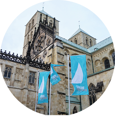 Der St.-Paulus-Dom in Münster aus der Seitenperspektiven. Neben dem Dom sind drei Fahnen-Masten mit Flaggen zum Katholikentag 2018 in den Boden eingelassen  (Harald Westbeld)