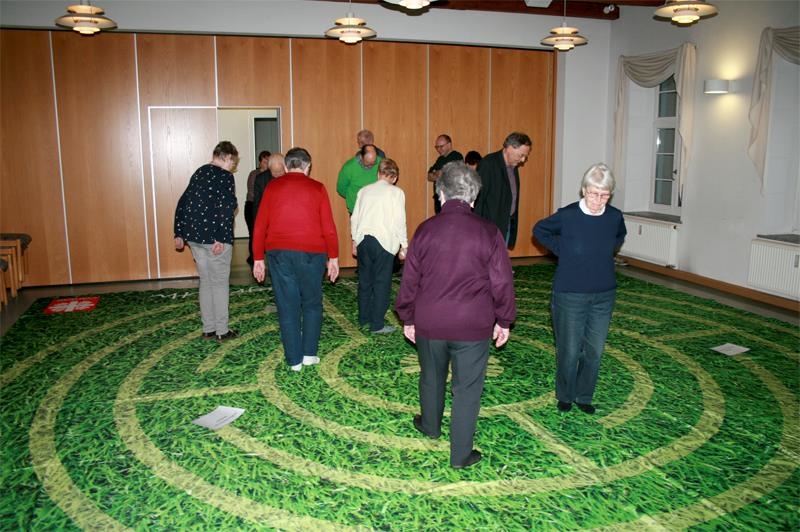 Menschen laufen über eine Matte, auf der in Labyrinth abgebildet ist 