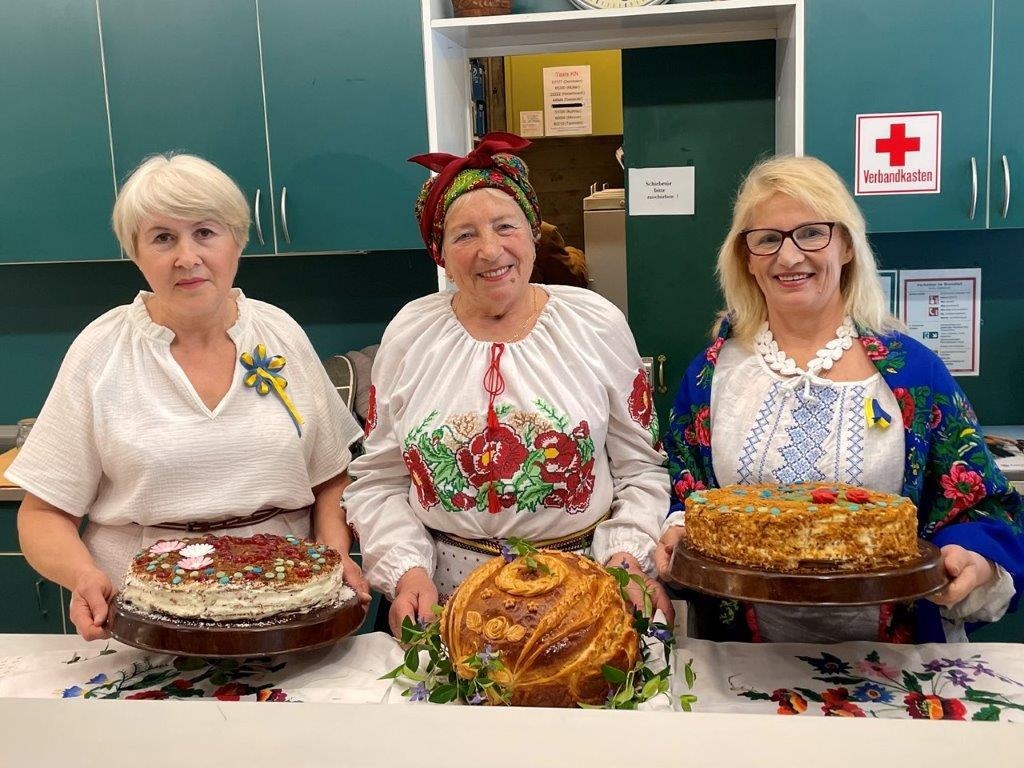 Drei Frauen in tradionellen ukrainischen Kleidern präsentieren ihre Kuchen. (Caritas Konstanz)