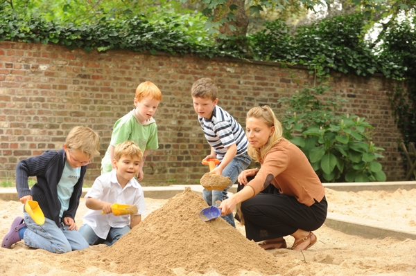 Kinder spielen mit einer Frau im Sand