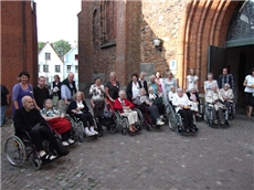 Eine Gruppe von Bewohnern im Rollstuhl mit Begleiterin vor der Kirche.