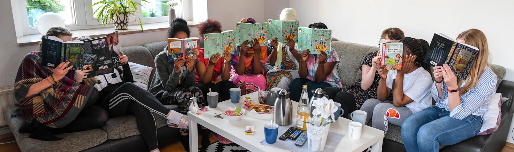 Fünf geflüchtete Mädchen halten sich Lesebücher vor ihre Gesichter