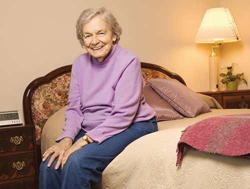 Seniorin sitzt lächelnd auf einem Bett / Foto: fotolia.de