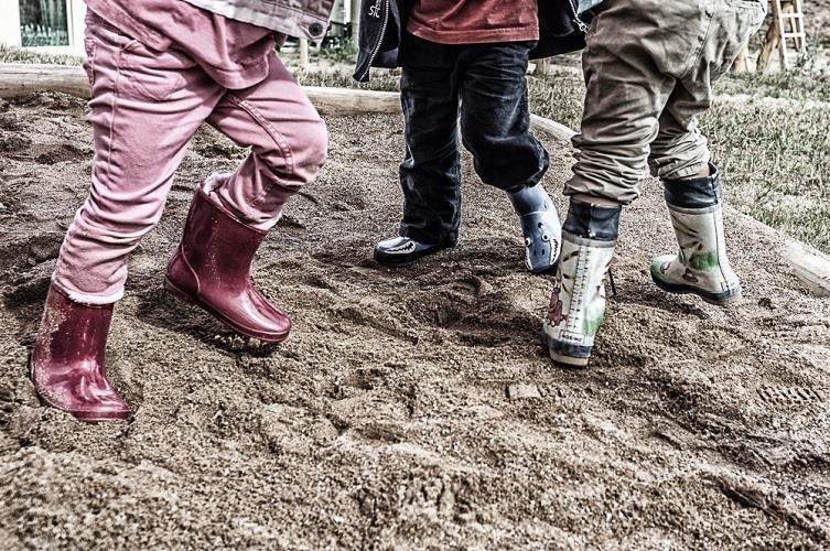 Beine und Füße von drei Kinder mit Gummistiefeln in einem Sandkasten (HAUS TOBIAS/Caritasverband Trier)