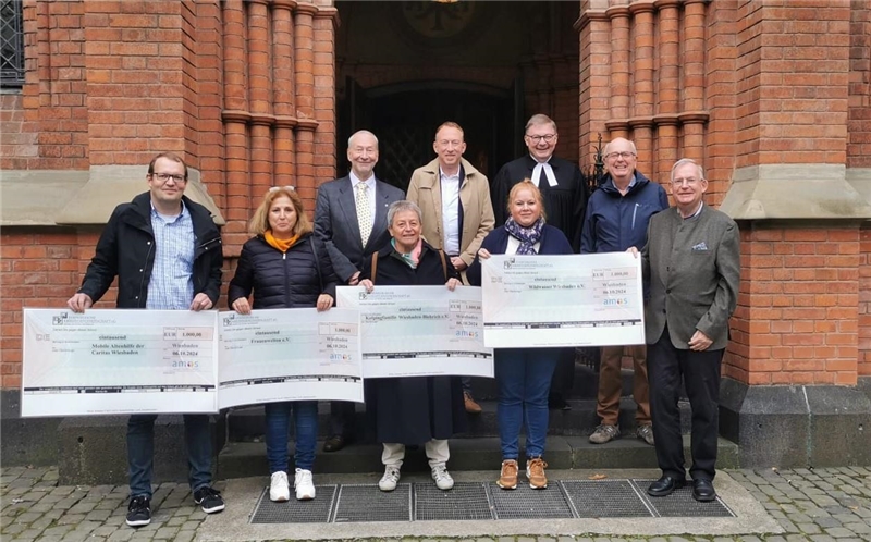 Vorne stehen die vier Preisträger mit großen Symbolschecks auf der Eingangstreppe der Bergkirche. Eine Stufe darüber stehen die vier Verantwortlichen der Amos-Stiftung und der Pfarrer der Bergkirche.