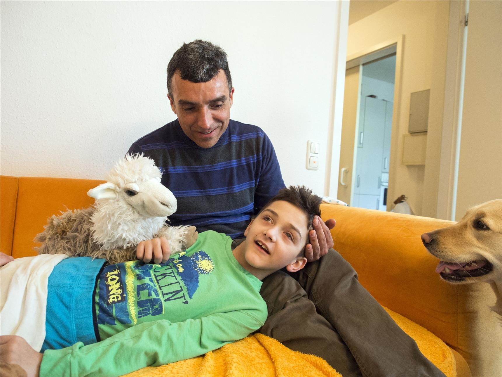 Behinderter Junge auf den Knien eines Mannes, der mit einem Stofftier spielt (Angela Kröll)