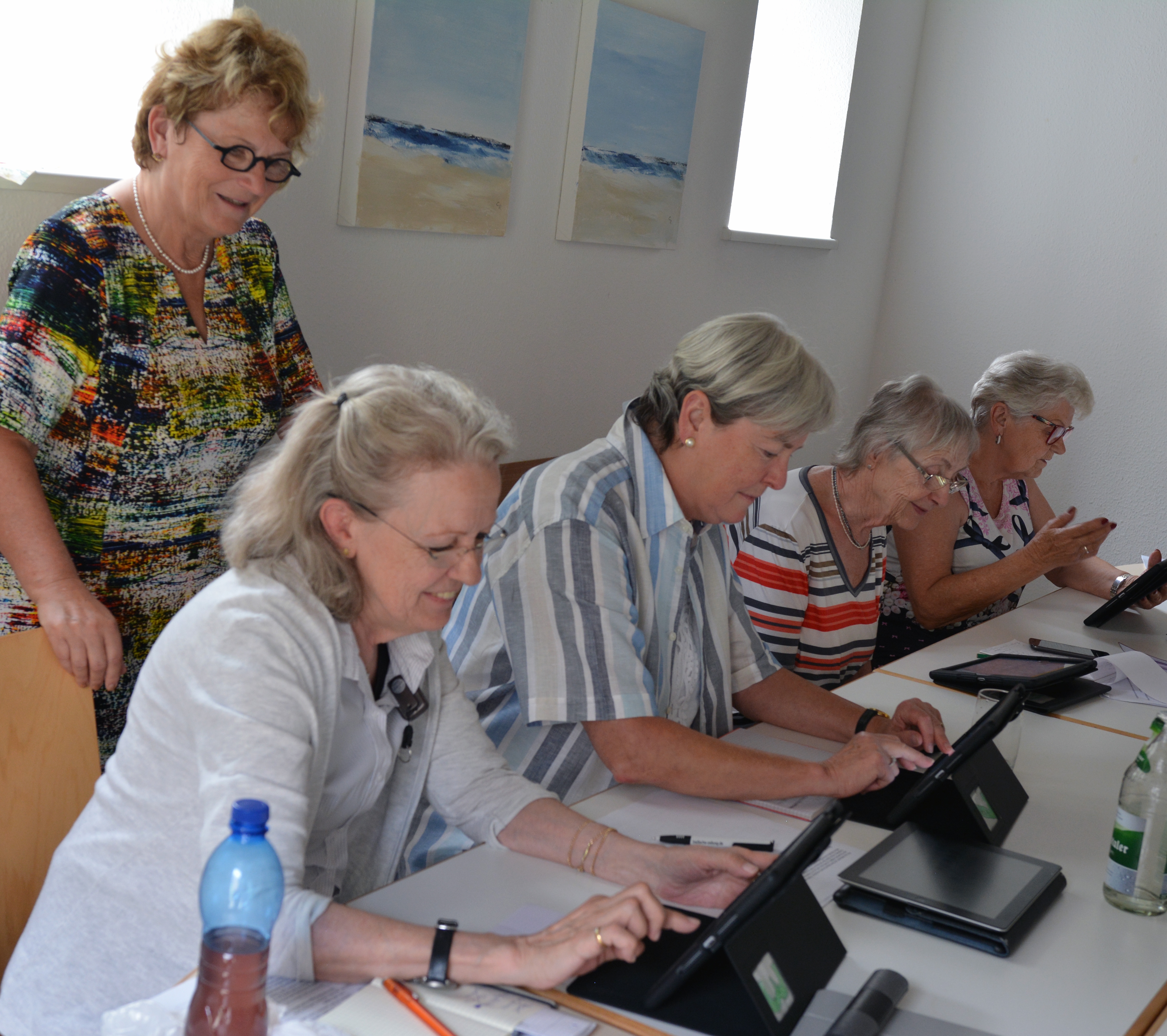 Vier Seniorinnen sitzen vor Tablets und machen sich mit den Fuktionen vertraut. Über die Schulter schaut ihnen Kursleiterin Erika Tischer-Oberdorf