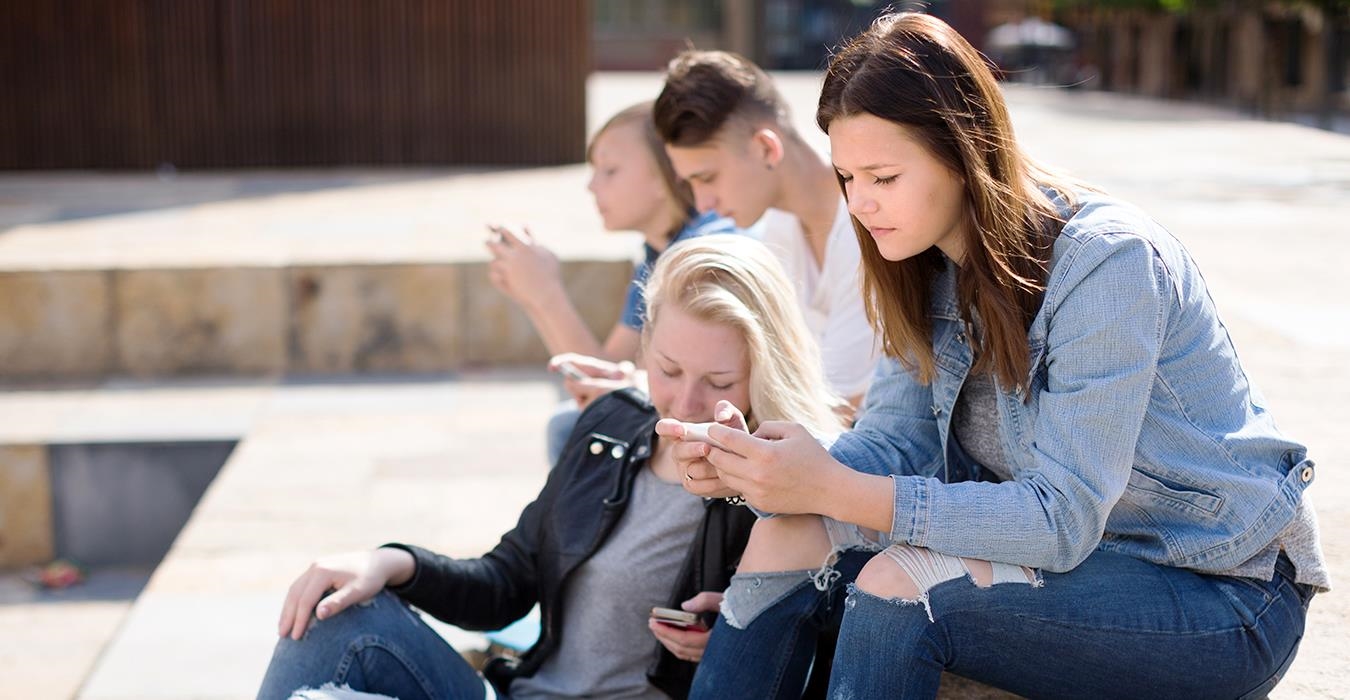 Schülerinnen und Schüler sitzen auf Freitreppe und sind mit ihren Smartphones beschäftigt.