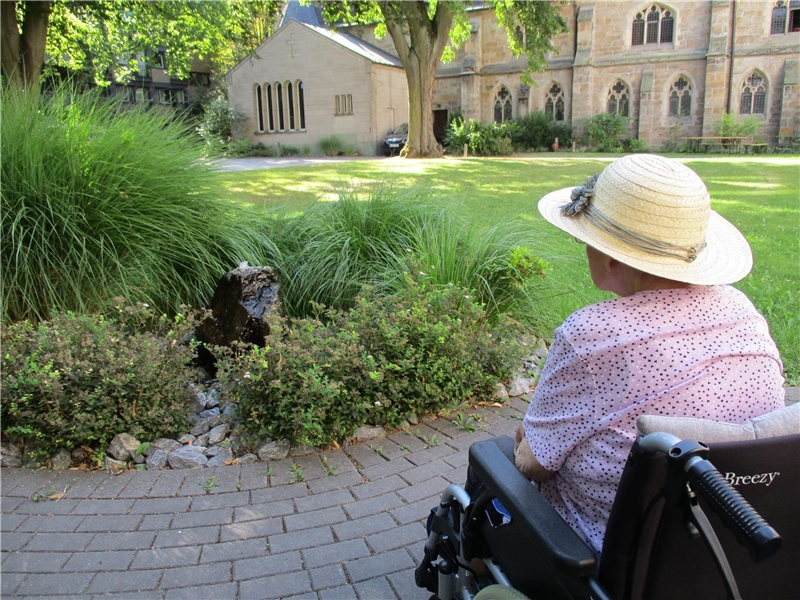 Eine Frau sitztim Rollstuhl im Klostergarten, der an das Bruder Jordan haus grenzt.