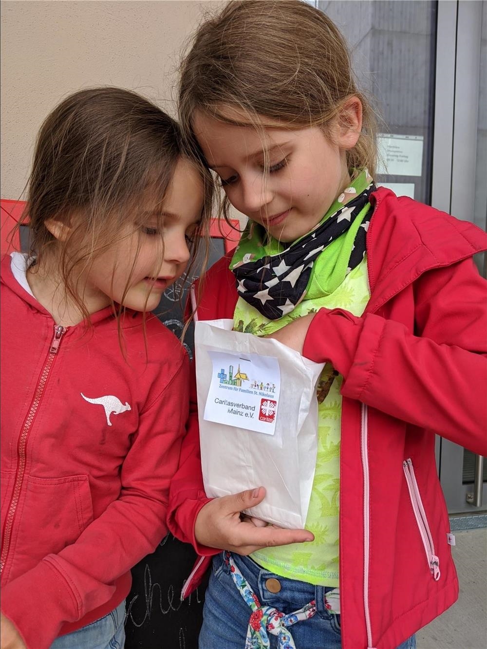 Zwei Mädchen gucken neugierig in eine mit Überraschungen gefüllte Butterbrottüte (Foto: Caritas Haus St. Rochus, Mainz)
