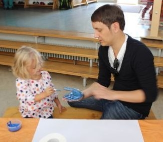 Ein Kind pinselt seinem Vater die Hand mit blauer Farbe ein. (Cordula Bösmüller, Kita St. Elisabeth Großheubach)