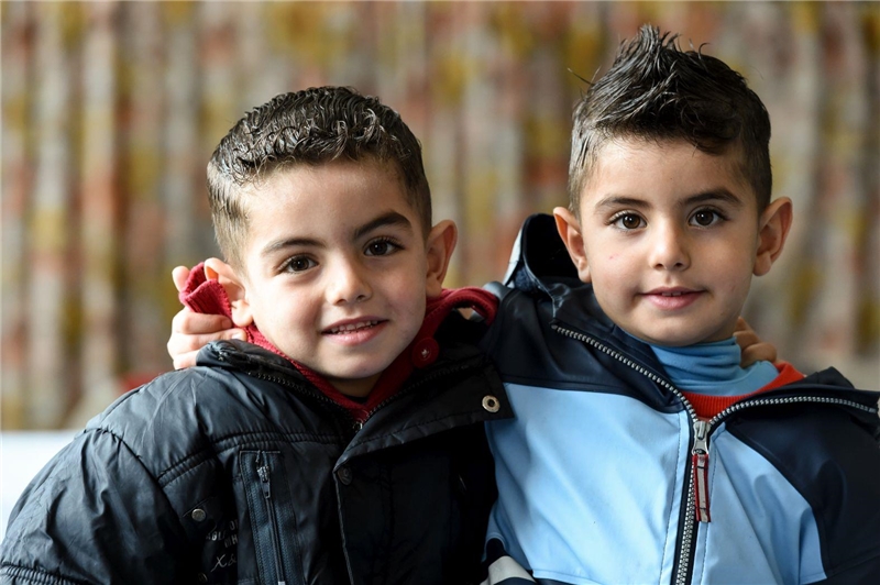 Zwei Jungs mit Migrationshintergrund halten sich im Arm und blicken in die Kamera