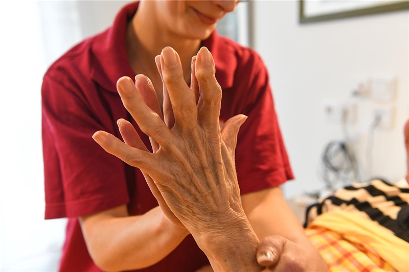 Pflegerin und ältere Dame legen liebevoll ihre Hände übereinander