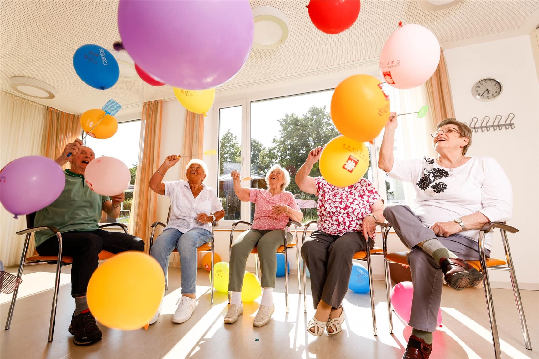 Senior:innen sitzen in einem Stuhlkreis und werfen sich Luftballons zu. 