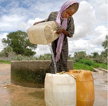 Eine junge Frau füllt in einem afrikanischen Land Trinkwasser aus einem Brunnen in Kanister.
