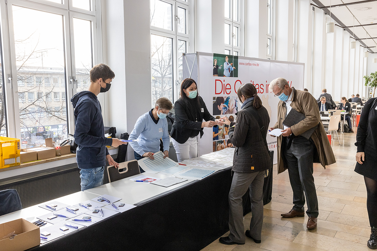 Drei Teilnehmende melden sich im Foyer bei drei Mitarbeitenden zum  1. Kath. Krankenhaustag NRW am 10.11.2021 in Essen an (Foto: Achim Pohl)
