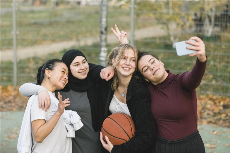 Gruppe von Mädchen im Teenageralter, die Selfies auf dem Basketballplatz machen