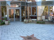 Hauseingang vom Innenhof mit reflektierender Glasfassade, Sitzgruppe und Blumenkübeln / Astrid Heyer