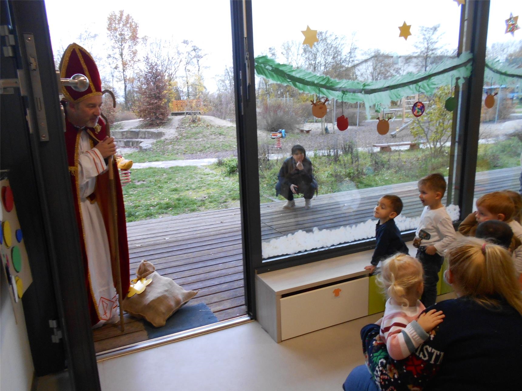 Bischof Nikolaus steht vor der offenen Tür der Kita Arche Noah und blickt auf die wartenden Kinder